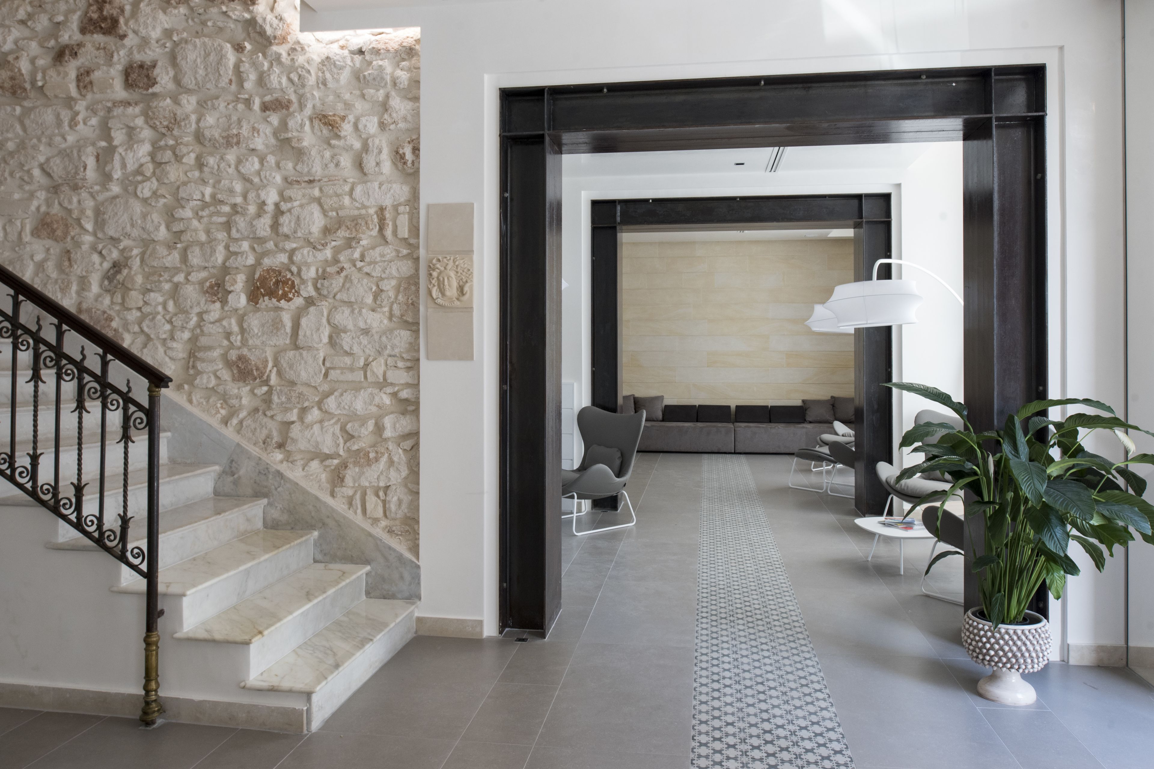 A modern interior with a stone wall, a staircase, a seating area with a lamp, and a potted plant.
