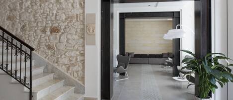 A modern interior with a stone wall, a staircase, a seating area with a lamp, and a potted plant.