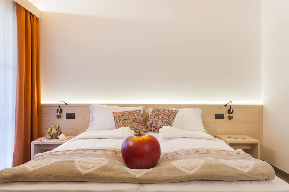 A neatly made bed with a large apple centerpiece, a wooden headboard, and a bedside table with a lamp.