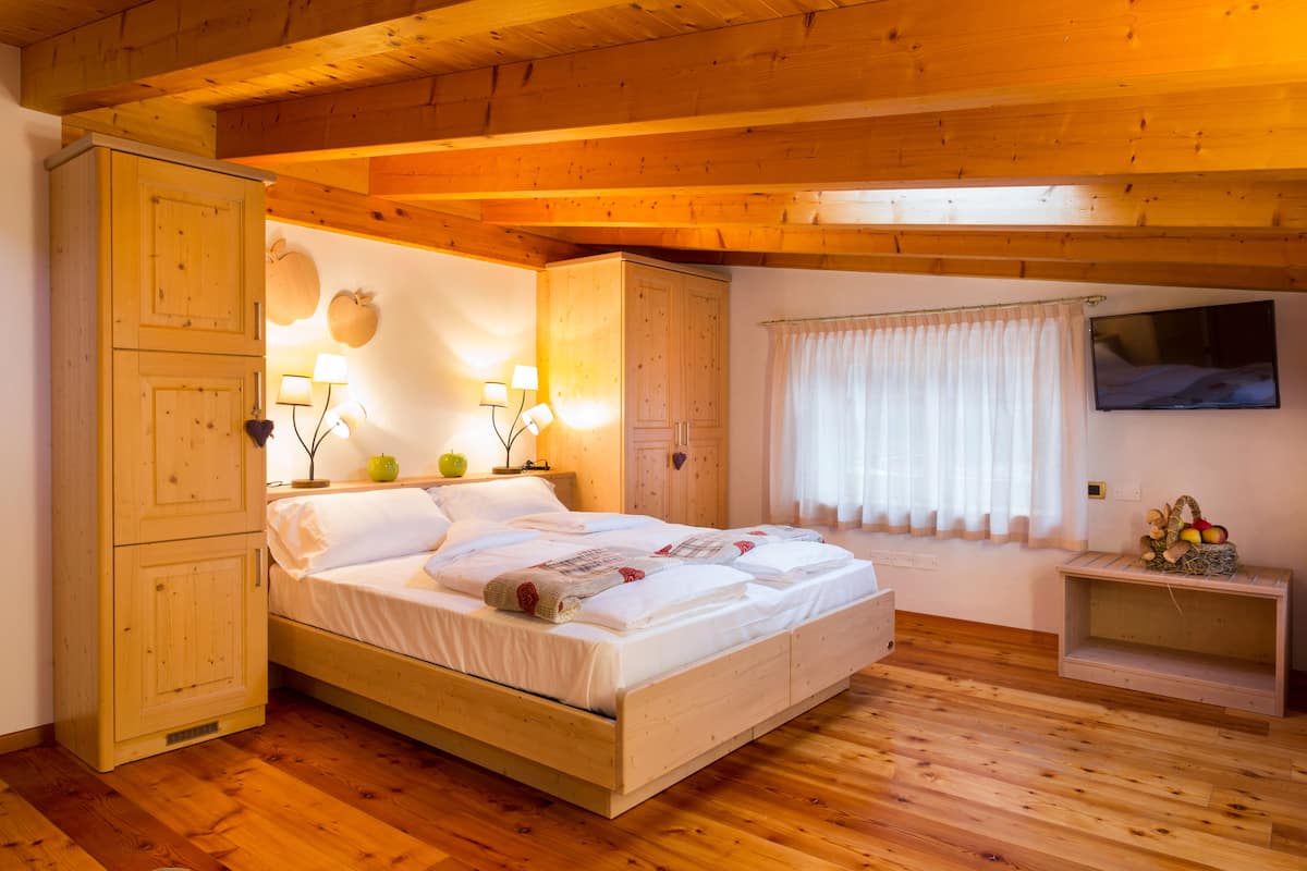 A wooden bedroom with a bed, a wardrobe, a nightstand, and a small table with fruit.