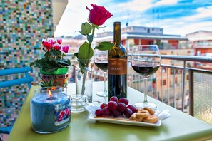 A table with a bottle of Syrah wine, a glass of wine, a plate of grapes, a candle, and a vase with pink flowers. - Oasi Verde a San Pietro (Rome)