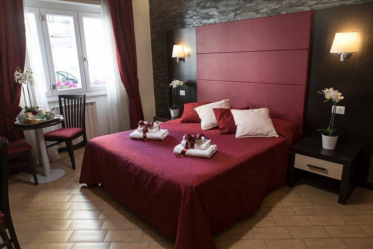 Ein Hotelzimmer mit einem großen Bett, zwei Nachttischen, einem Sessel, einem kleinen Tisch mit Lampe und einem Fenster mit Vorhängen.
