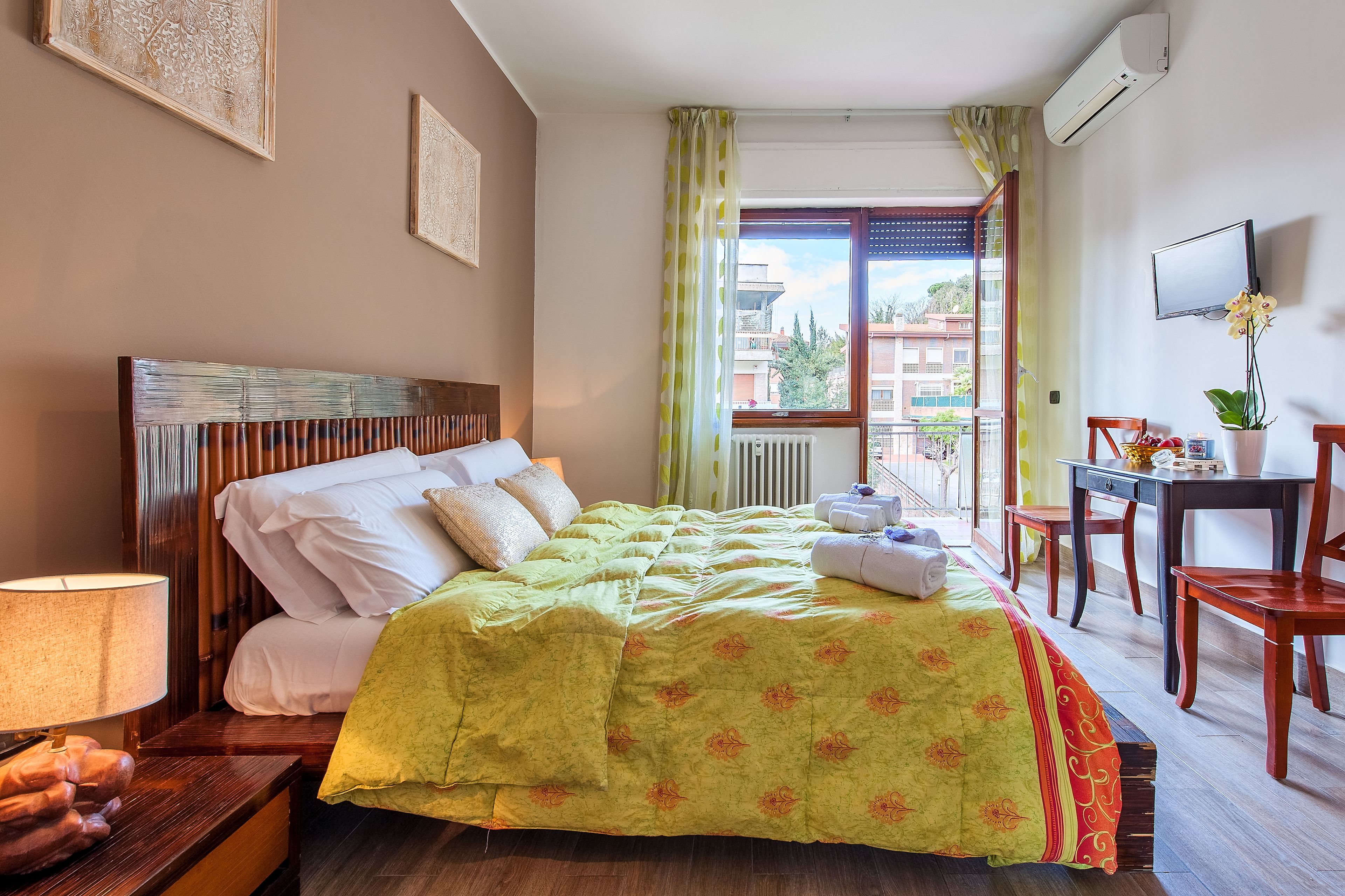 Ein Hotelzimmer mit Bett, Schreibtisch, Stuhl, Fernseher und Fenster mit Blick auf Gebäude.