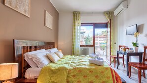 A hotel room with a bed, a desk, a chair, a TV, and a window with a view of buildings. - Oasi Verde a San Pietro (Rome)