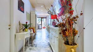 A hallway with a marble floor, a white console table with a statue, a potted plant, and a vase with flowers. - Oasi Verde a San Pietro (Rome)