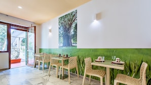A dining area with a large mural of a tree, wicker chairs, and a glass table with a green backdrop. - Oasi Verde a San Pietro (Rome)