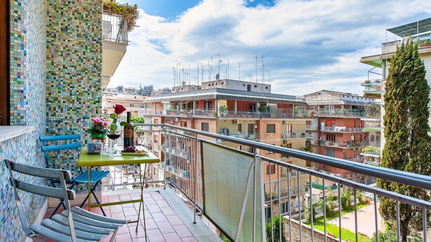 A balcony with a tiled wall, a table with a vase of flowers, and a chair. - Oasi Verde a San Pietro (Rome)