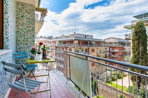 A balcony with a tiled wall, a table with a vase of flowers, and a chair. - Oasi Verde a San Pietro (Rome)