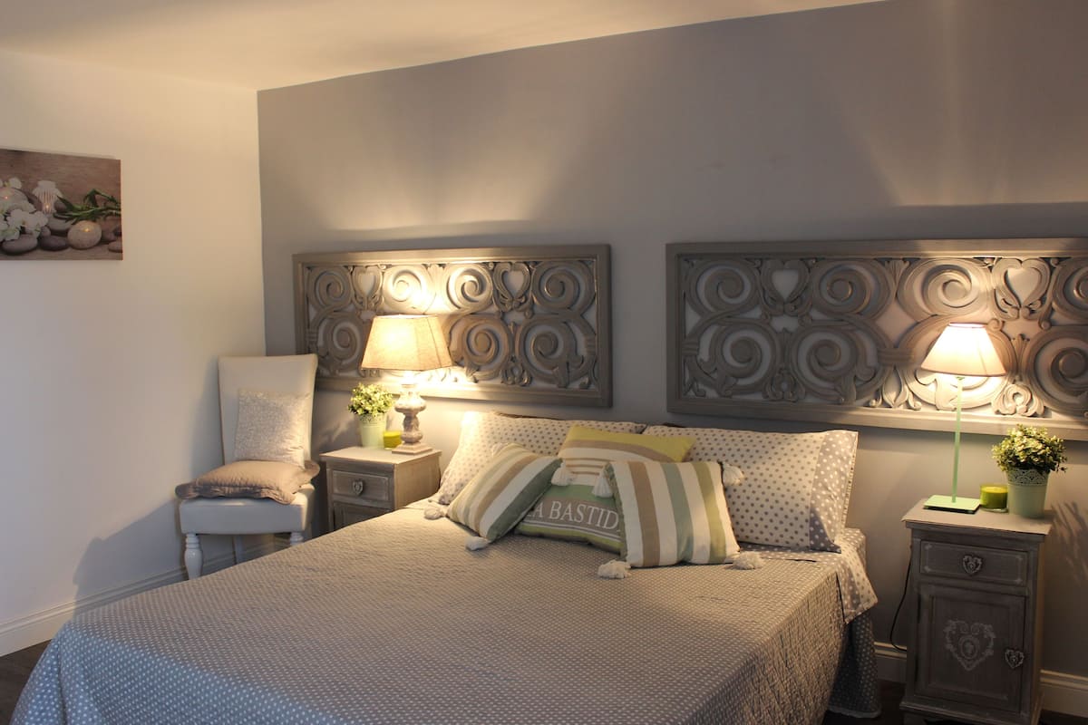 A bedroom with a bed, two nightstands, a chair, and decorative wall panels.