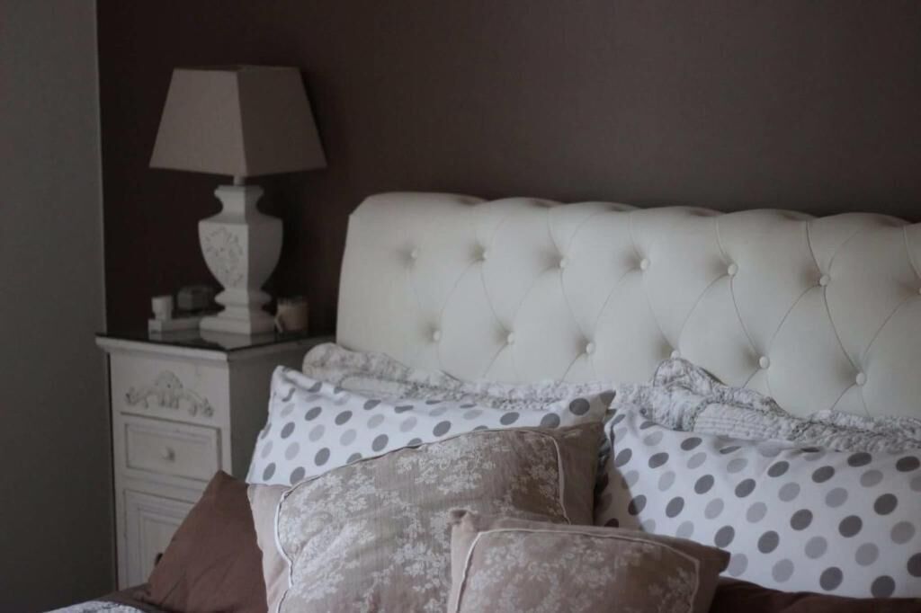 A bedroom with a tufted headboard, a bedside table with a lamp, and a dresser.