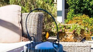 A wicker basket with a handle, placed on a patio with a cushion and a wooden fence in the background. - Le Lanterne B&B (Rome)