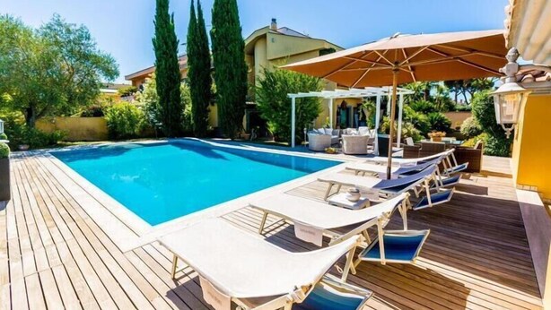 A poolside area with lounge chairs and umbrellas, surrounded by greenery and a building in the background. - Le Lanterne B&B (Rome)