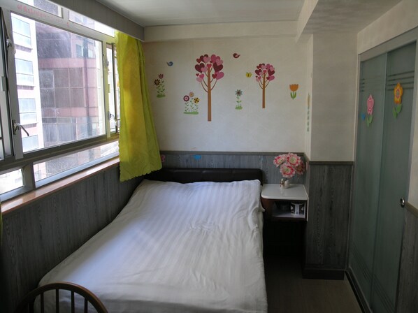 Un dormitorio con cama, mesita de noche, ventana con cortina y pared decorada con motivos florales.