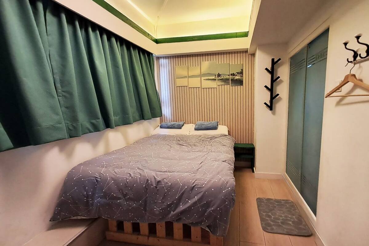 Ein Schlafzimmer mit Bett, Holz-Kopfteil, kleinem Tisch, Kleiderhaken und Blick auf eine Landschaft durch ein Fenster.