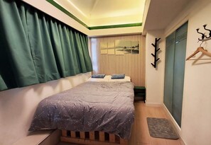 Une chambre à coucher avec un lit, une tête de lit en bois, une petite table, un porte-manteau mural et une vue sur un paysage par la fenêtre.