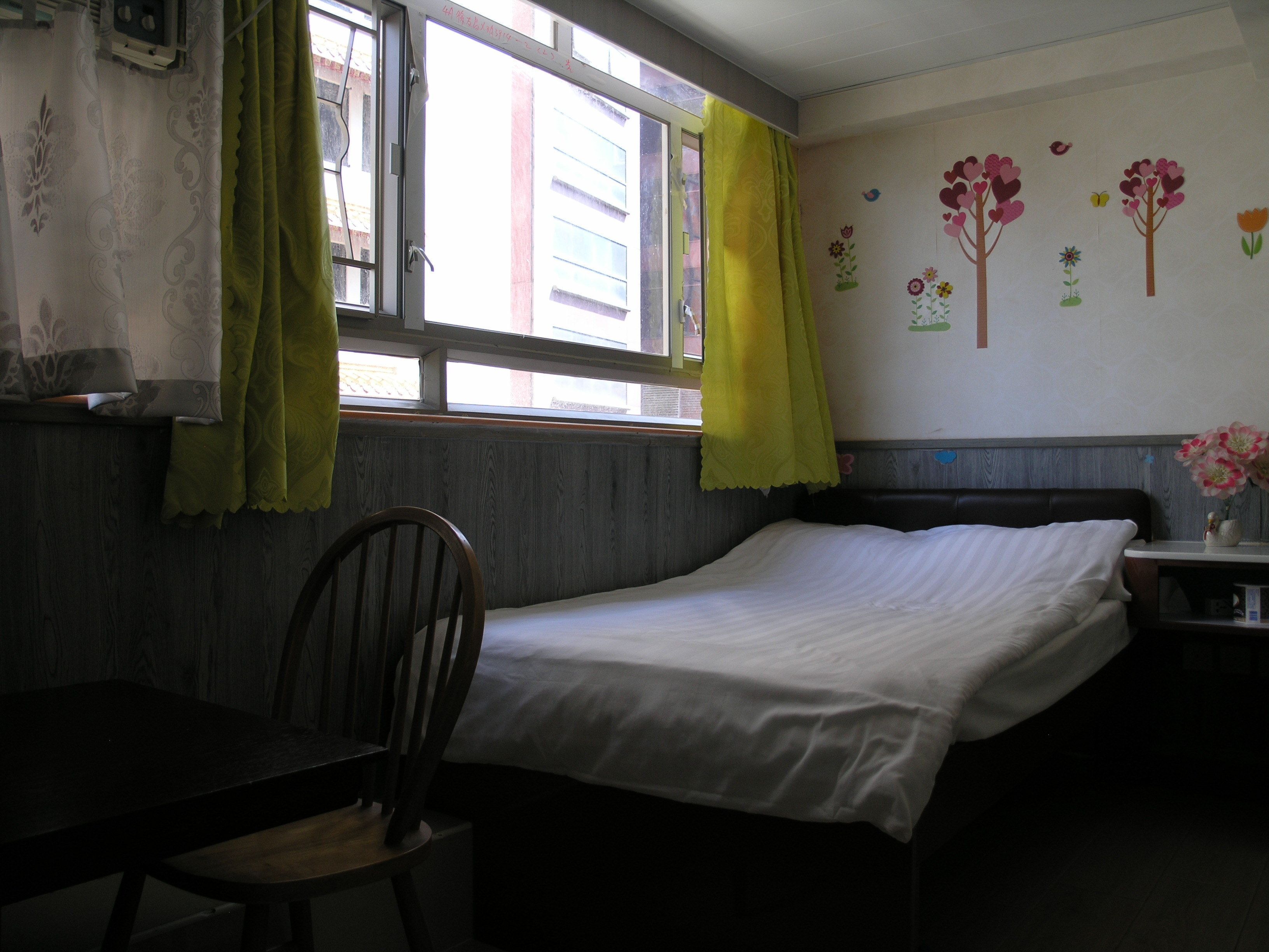 A room with a bed, a chair, a window with curtains, and a wall with a floral mural.