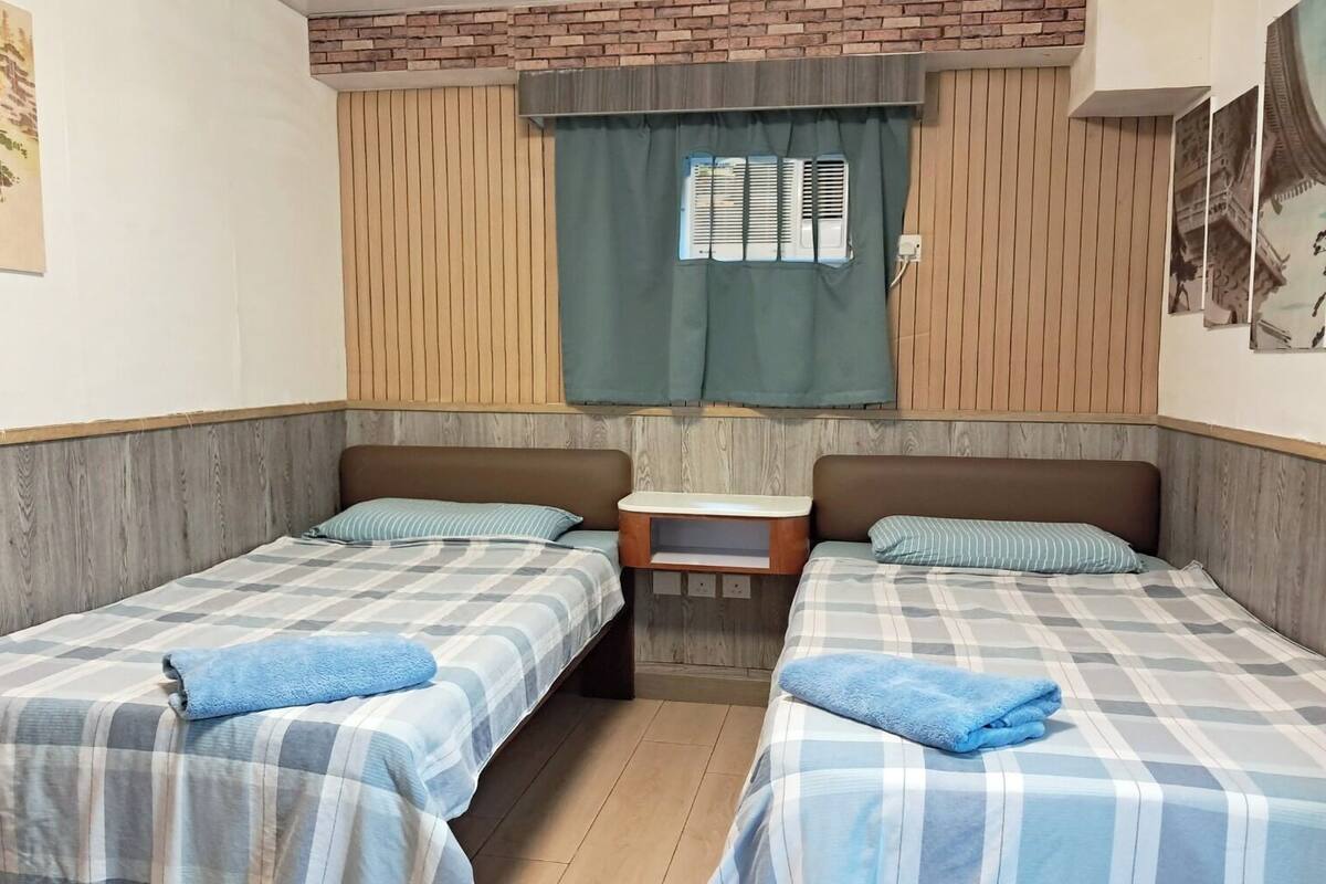Ein Zimmer mit zwei Betten, einem kleinen Tisch und einem Fenster mit Jalousien.