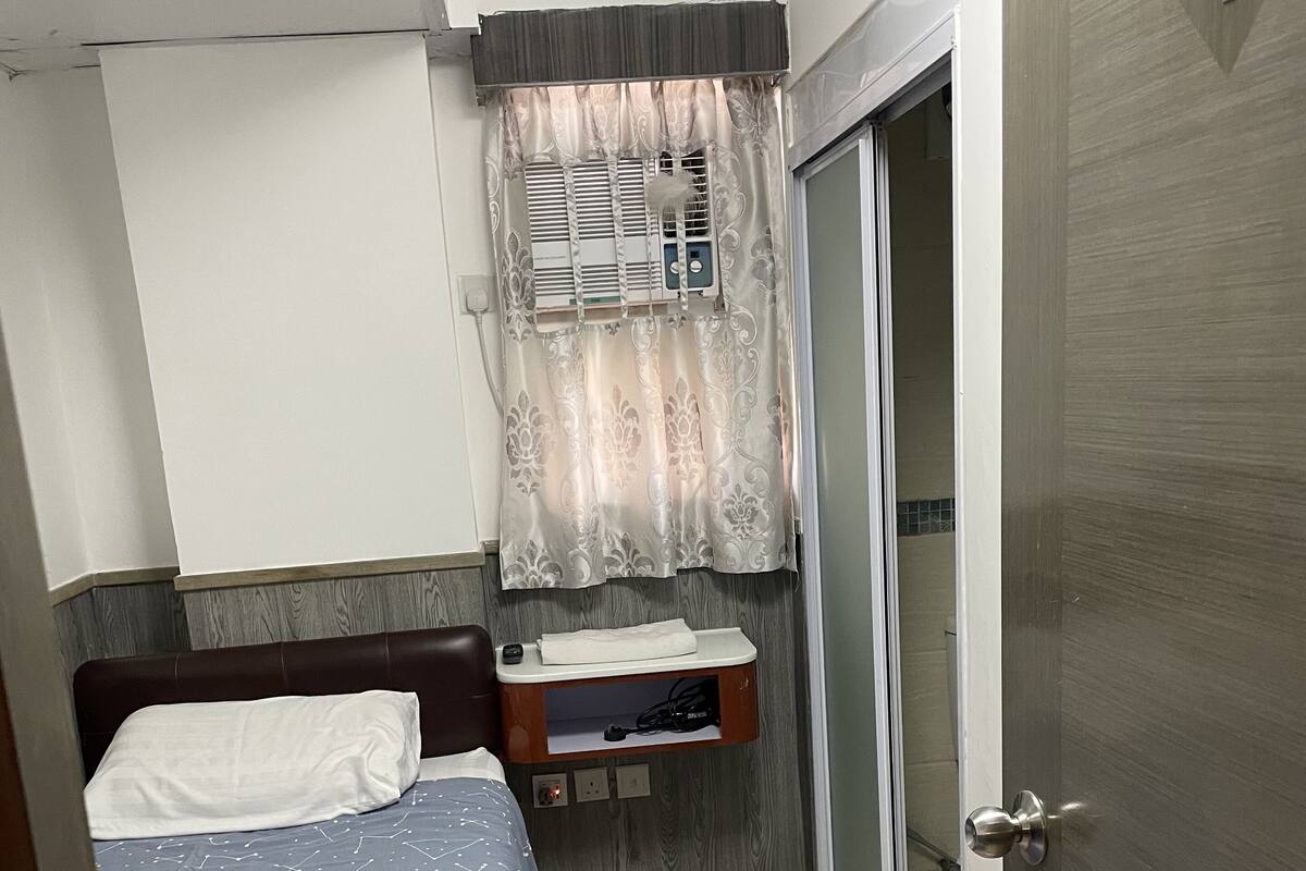 Ein kleines, aufgeräumtes Schlafzimmer mit einem Bett, einem Nachttisch, einem Fenster mit Vorhängen und einer Schiebeglastür.