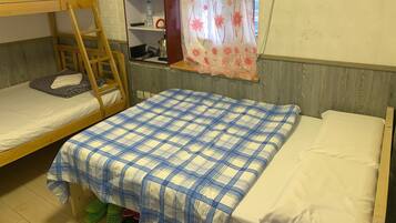 A dormitory room with bunk beds, a wooden ladder, a shelf with a vase of flowers, and a window with a floral curtain.