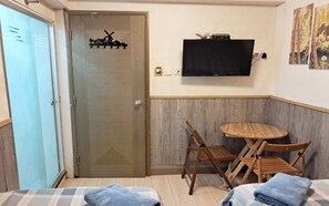 A room with a bed, a small table with chairs, a television mounted on the wall, and a door with a windmill decoration. - Majestic 7 Guest House (Kowloon)