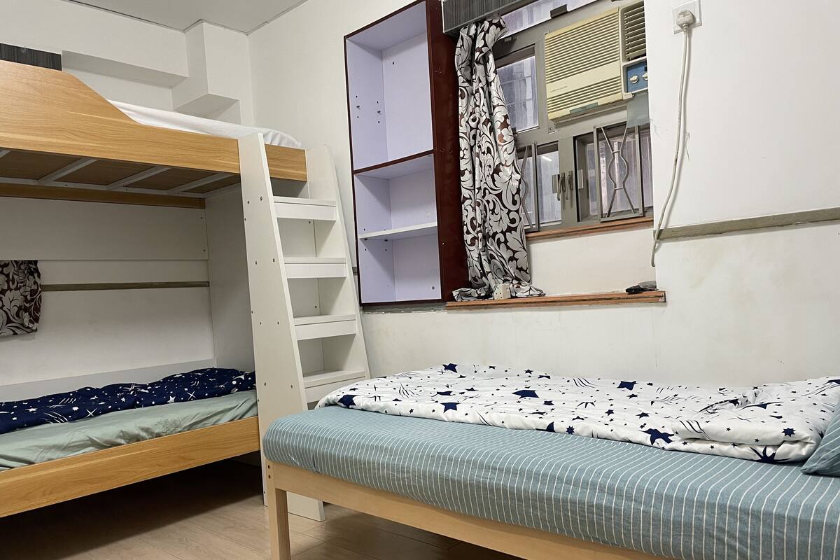 Ein Schlafsaalzimmer mit Etagenbetten, einem Fenster mit Vorhängen und einem Regal mit Büchern.