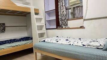 A dormitory room with bunk beds, a window with curtains, and a shelf with books.