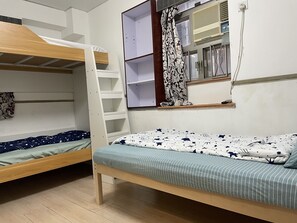 Une chambre de dortoir avec des lits superposés, une fenêtre avec des rideaux et une étagère remplie de livres.