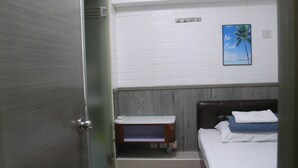 Une chambre d’hôtel avec un lit, une petite table de chevet, un téléviseur fixé au mur et une porte donnant sur une autre pièce.