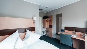 Habitación de hotel con cama, escritorio, silla, perchero y armario.