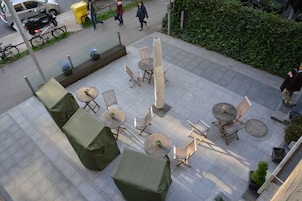 Un espacio al aire libre con mesas y sillas, una zona de estar cubierta y un pilar central.