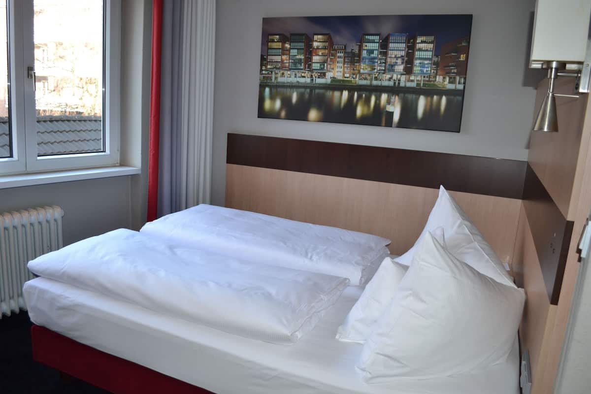 Cama bem arrumada com lençóis brancos em quarto de hotel.