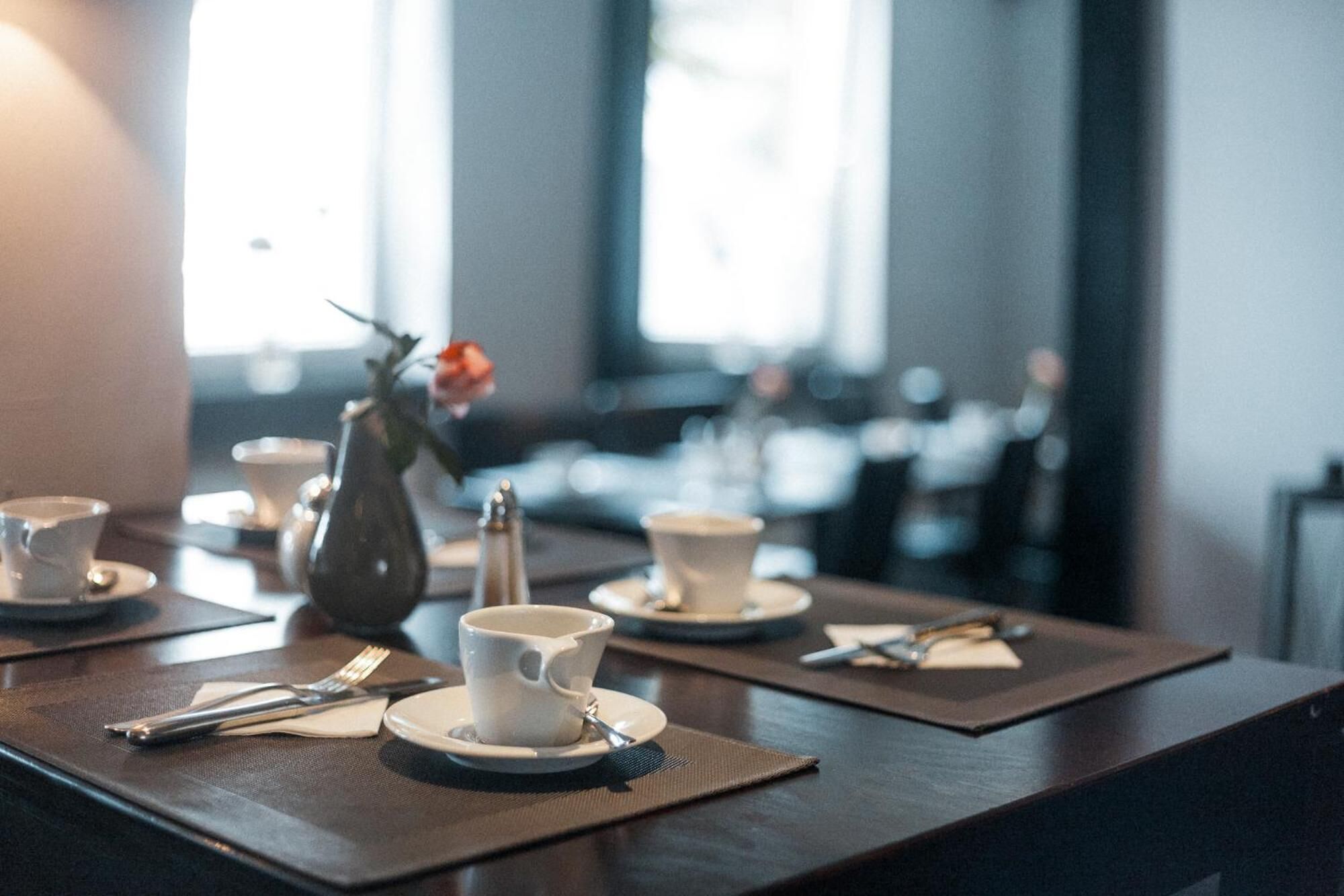 Un comedor con mesas dispuestas para una comida, incluyendo tazas, platillos y cubiertos.