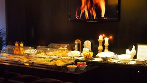 Dispositiu de buffet amb diferents plats, una televisió que mostra flames i espelmes sobre la taula.