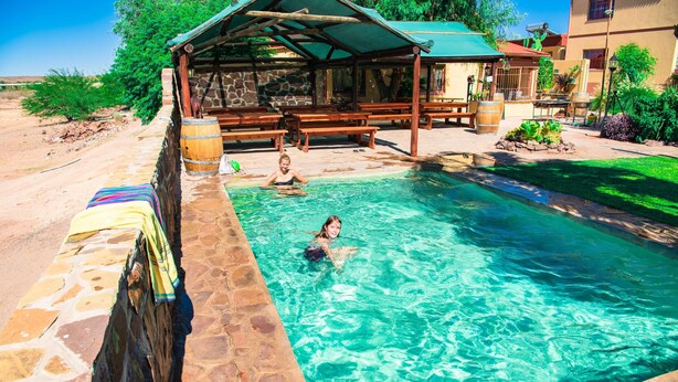 A swimming pool with stone walls and wooden benches. - Maltahohe Hotel (Maltahohe)