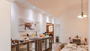 A modern kitchen with a central island, wooden cabinets, and a dining area with a table set for four. - Maltahohe Hotel (Maltahohe)