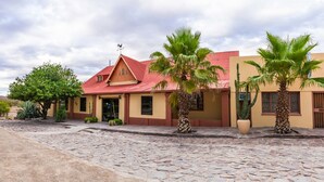 A building with a red roof, a weather vane, and palm trees in front. - Maltahohe Hotel (Maltahohe)