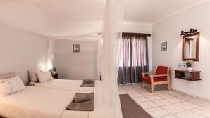 A hotel room with two beds, a red chair, a small table with a plant, and a mirror on the wall. - Maltahohe Hotel (Maltahohe)