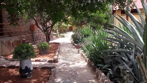 A stone pathway flanked by potted plants and cacti, leading to a building with a stone facade and red window frames. - Maltahohe Hotel (Maltahohe)