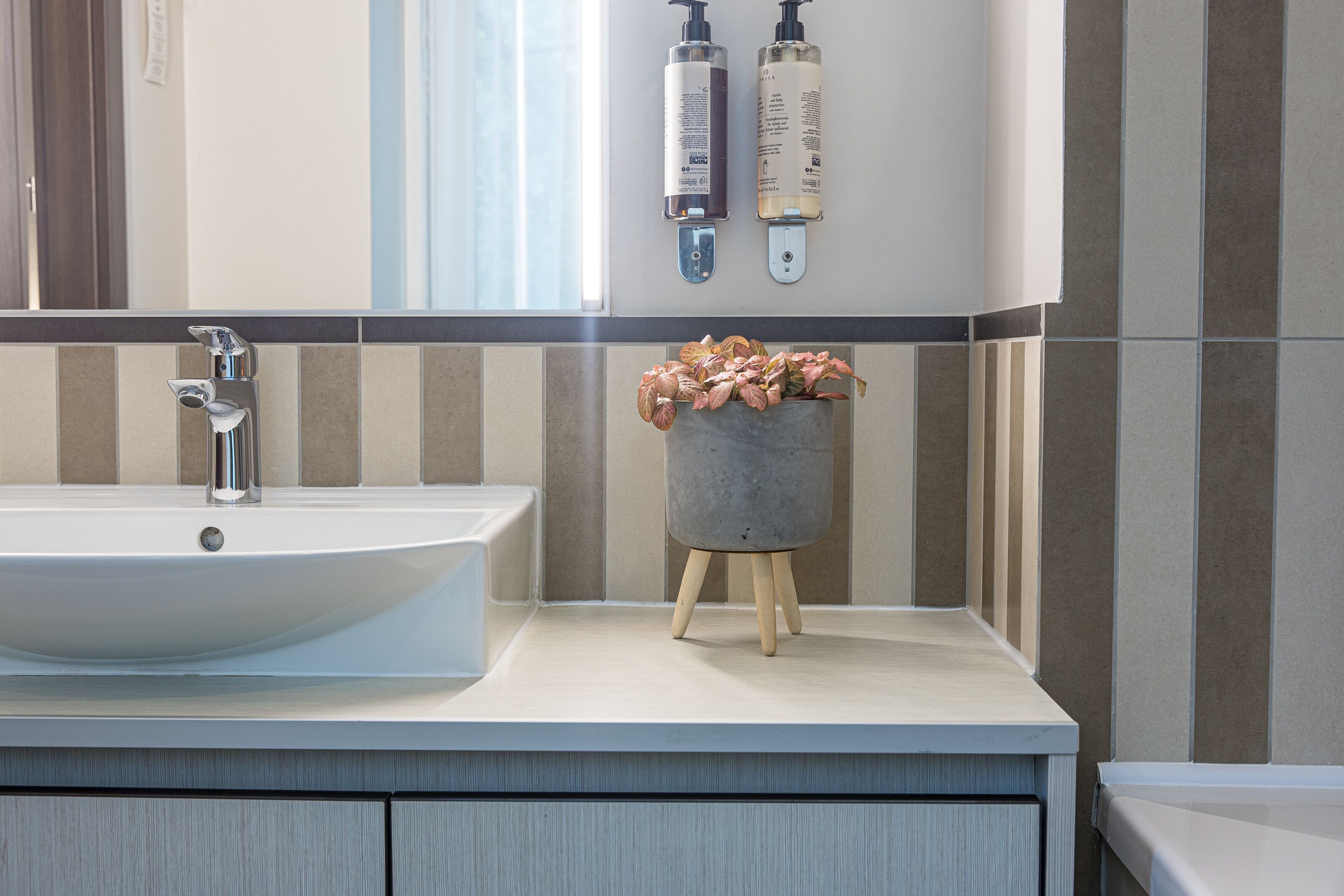 A bathroom with a large white sink, a mirror, and two bottles of shampoo on the wall.