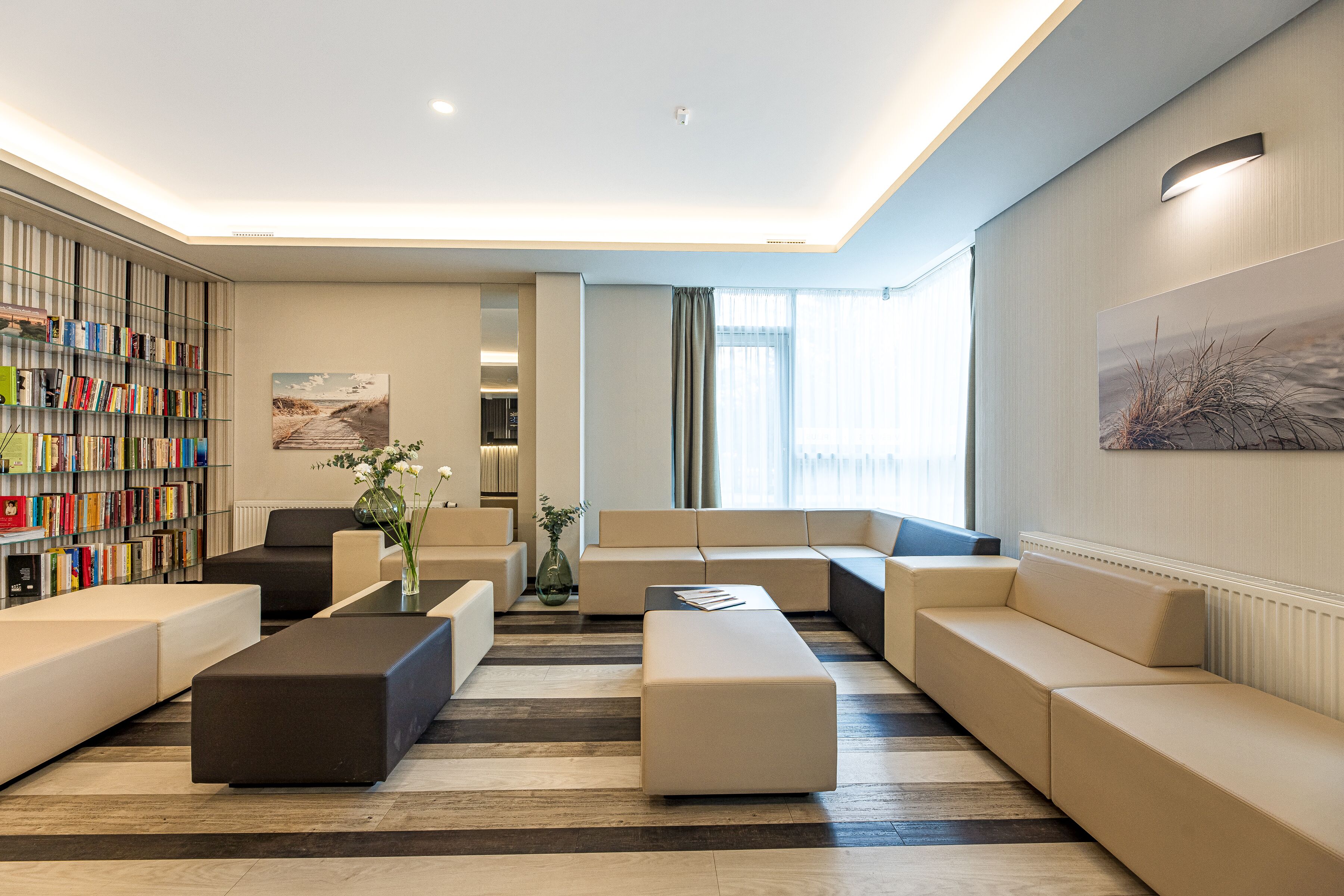 A modern living room with a bookshelf, sofas, and a large window.