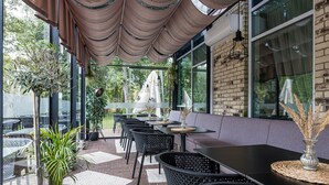 An outdoor patio with brick flooring, black metal chairs, and tables, featuring a brick wall and large windows. - Grand Baltic Dunes (Palanga)