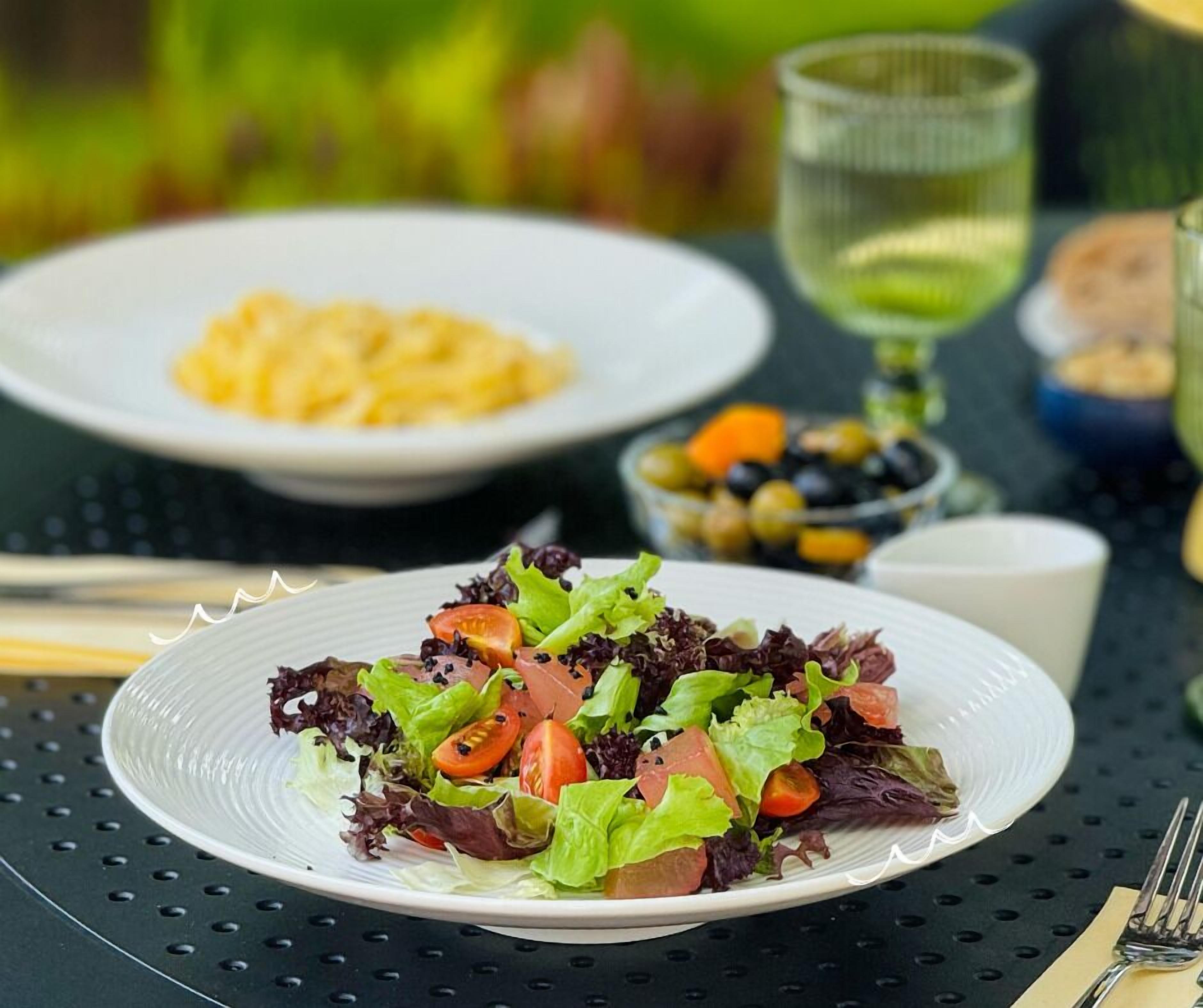 A table with a plate of salad, a plate of scrambled eggs, and a glass of green drink.