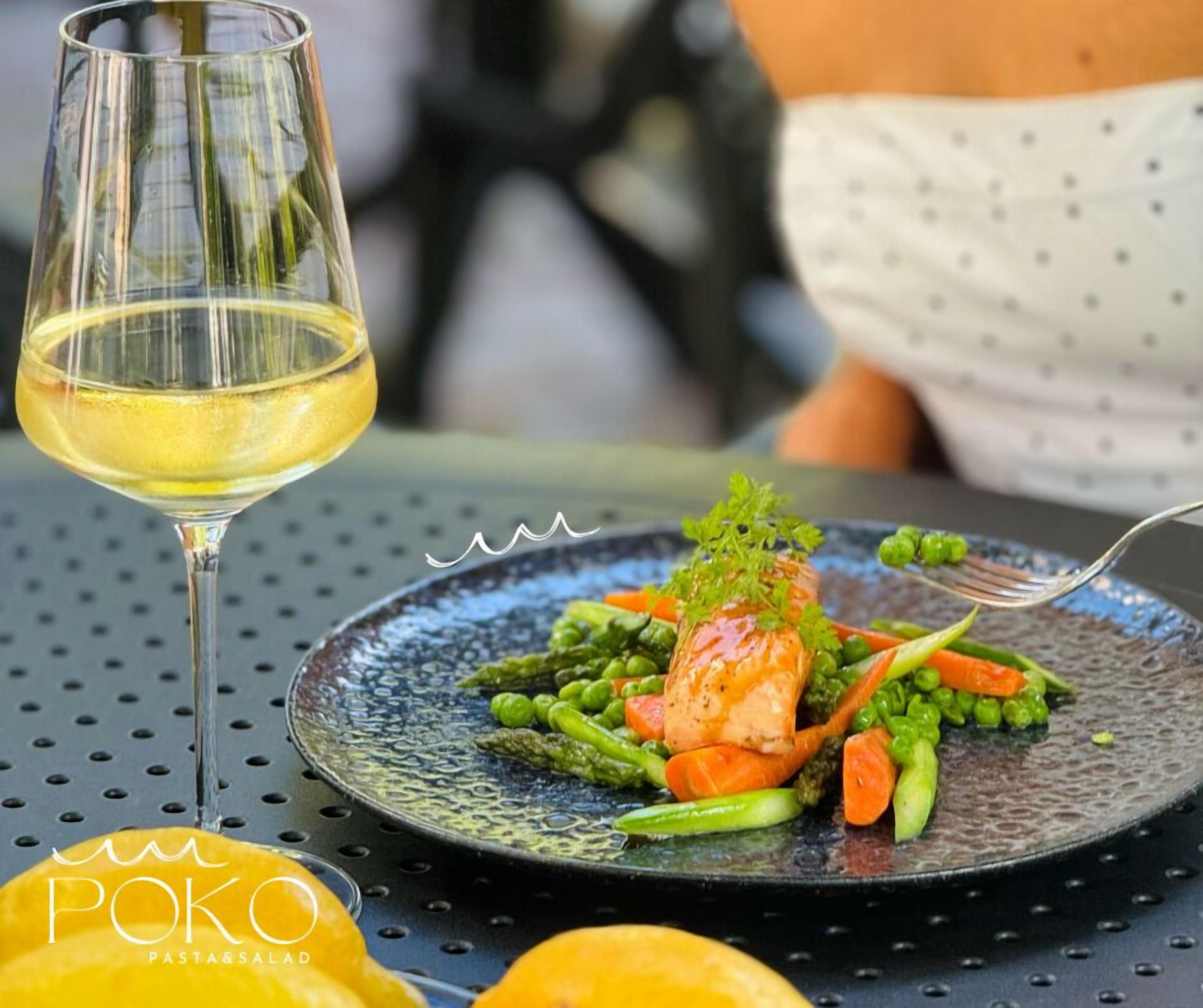 A dining table with a plate of food and a glass of white wine.