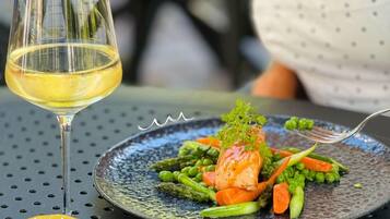 A dining table with a plate of food and a glass of white wine.
