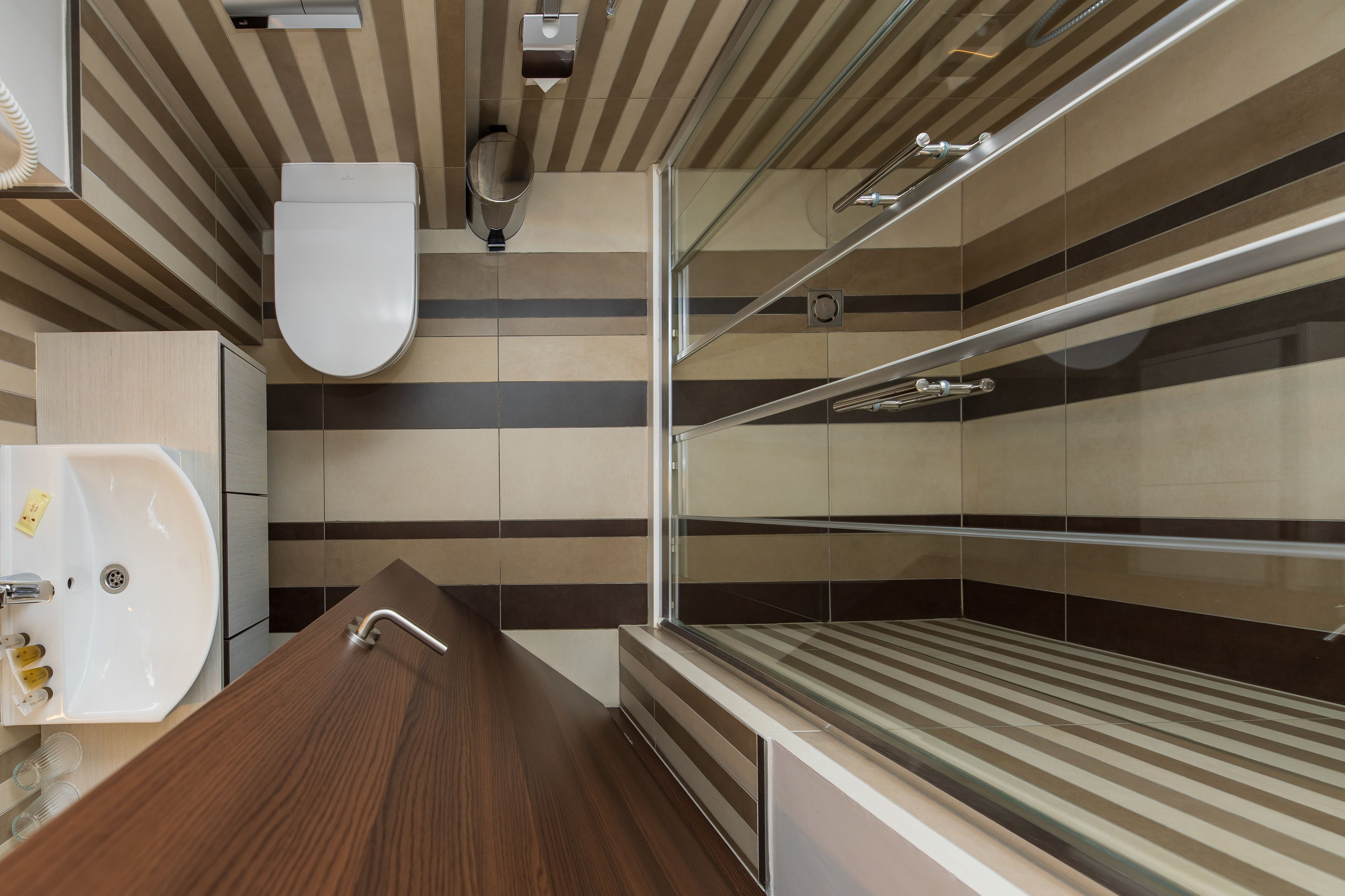A modern bathroom with a wooden vanity, a glass shower enclosure, and striped wall tiles.