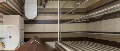 A modern bathroom with a wooden vanity, a glass shower enclosure, and striped wall tiles.