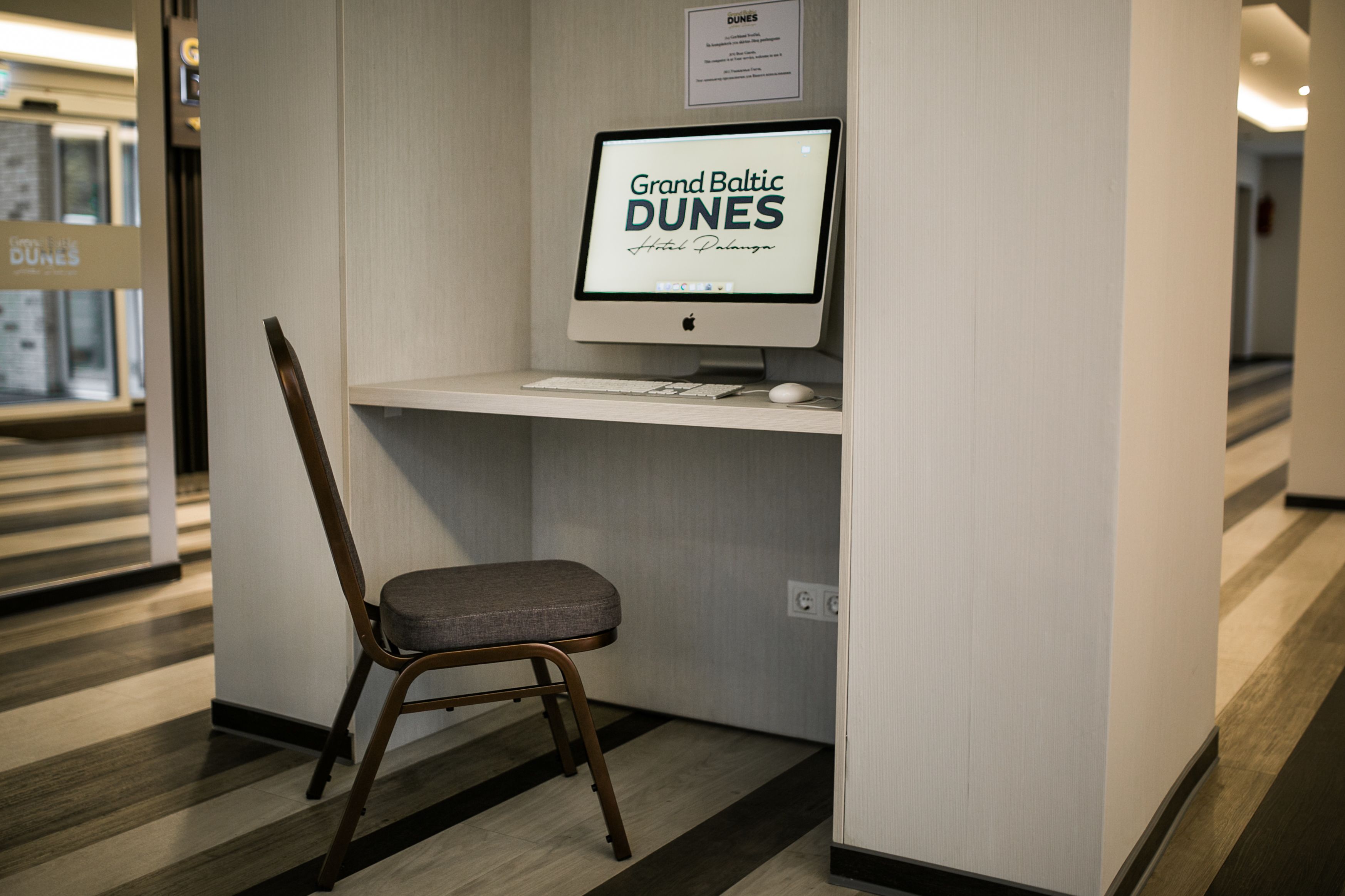A computer desk with a monitor, keyboard, and mouse, a chair, and a sign above the monitor.
