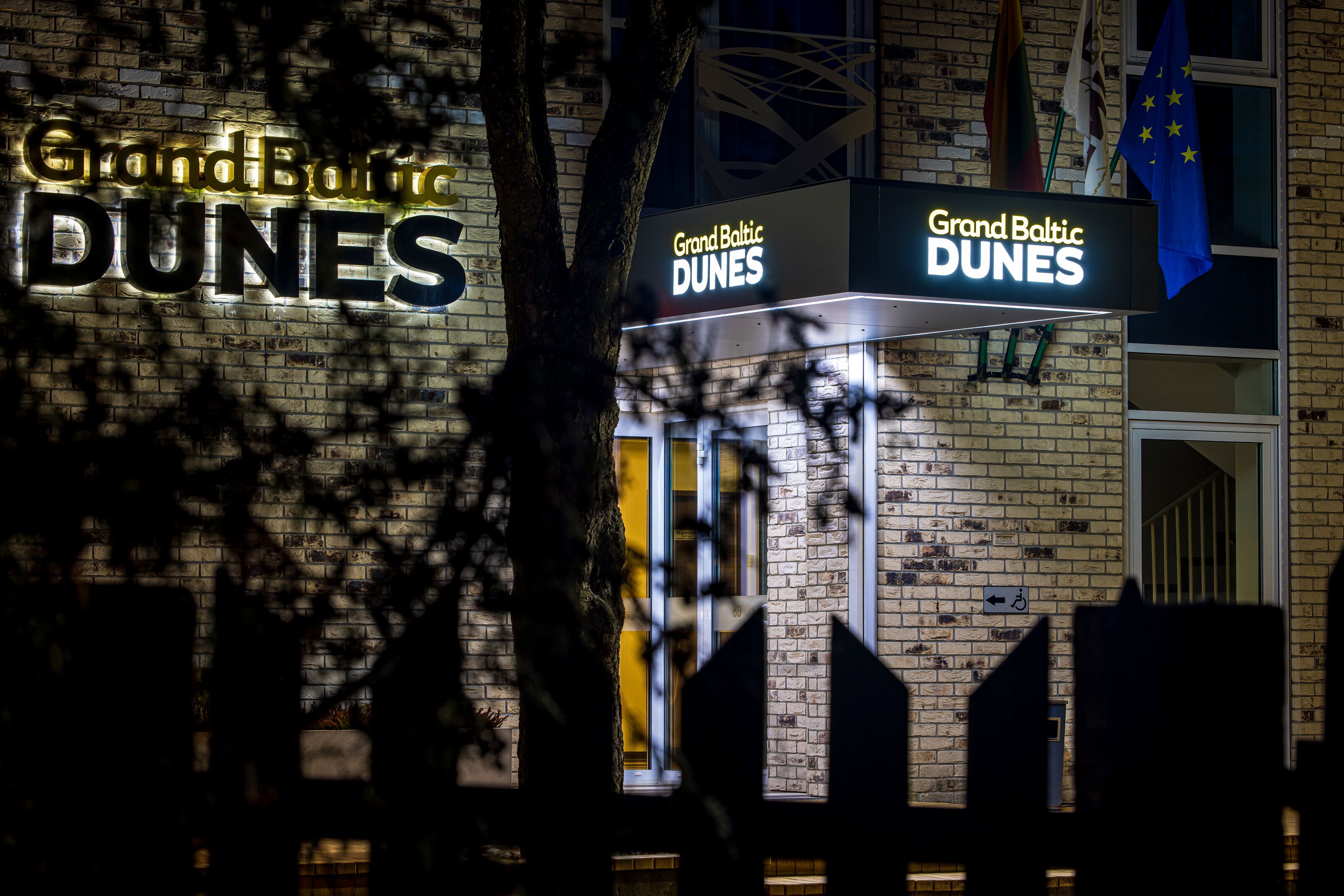 Señal de hotel con el nombre 'Grand Baltic Dunes' iluminado sobre un muro de ladrillo.