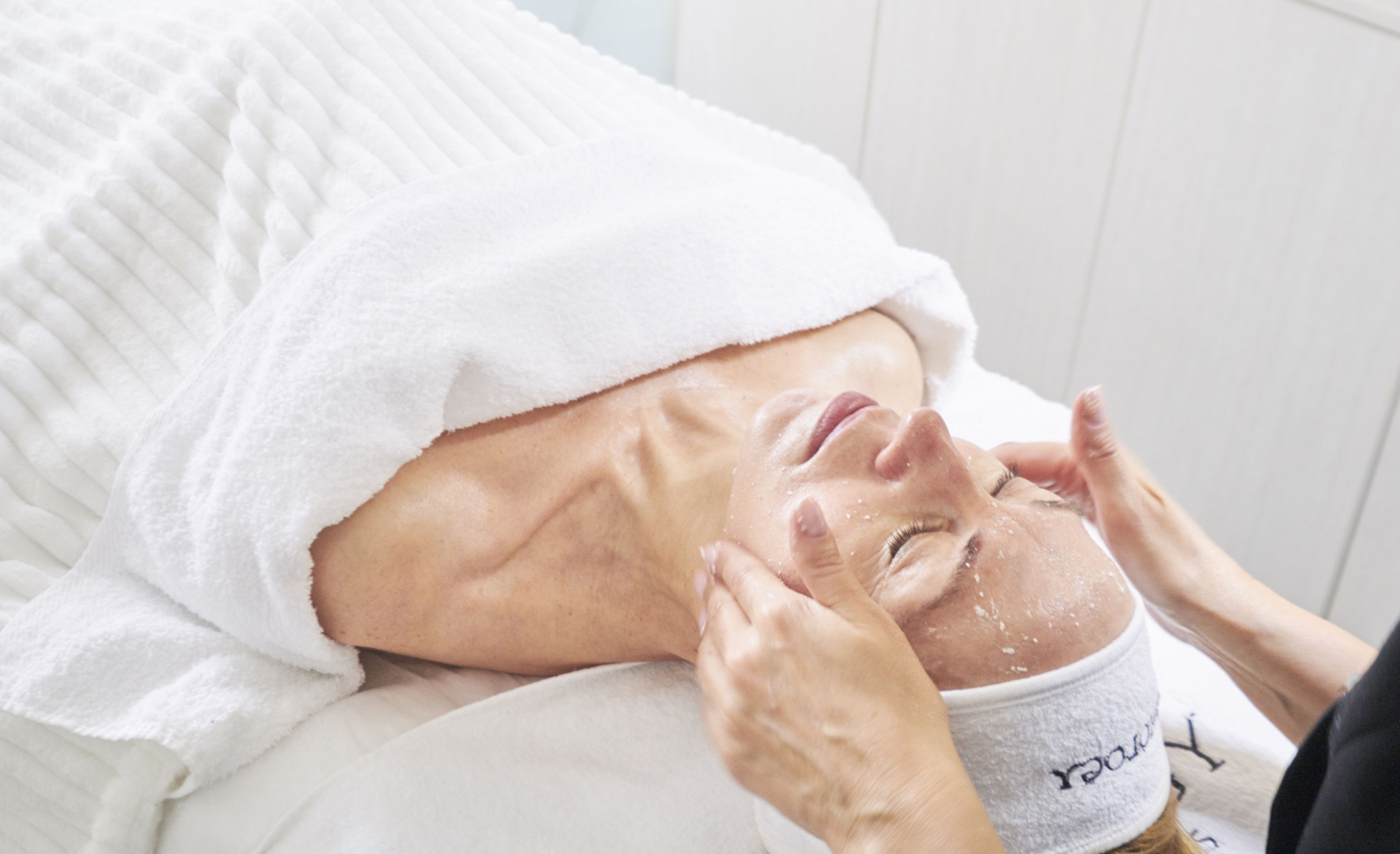 Una persona acostada con una toalla blanca cubriendo la cabeza, recibiendo un tratamiento facial.
