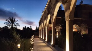 Un sendero con arcos que conduce a un edificio, rodeado de palmeras e iluminado con luces en el suelo.